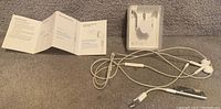 Apple 4GB iPod Shuffle with earphones, original clear plastic case and user manual on a gray surface.