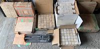 Seven boxes and one tile cutting tool arranged on the floor. Boxes contain different types of new tiles, including mosaic and large format tiles.