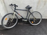 Full side view of black Staccato men's mountain bike with knobby tires, shows bike frame, pedals, and both tires, rear tire is visibly flat.