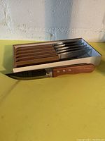 Photo of six steak knives lined up in a white box showing wooden handles and stainless steel blades