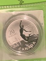 Close-up of silver coin in protective plastic casing showing boy jumping into water design, '20 DOLLARS', '2014', 'CANADA' and fine silver purity markings.