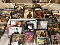 Overview of 107 vintage CDs arranged on table in original jewel cases, visibly including Santana, Twisted Sister, Joshua Radin, Randy Travis, and The Mermen albums.
