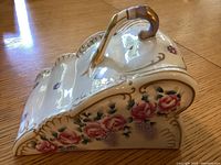 Side angle showing floral painted decoration with pink roses, grapes and gold trim detail on the cheese keeper.