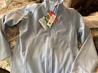 Front view of new light blue Black Diamond jacket laid flat showing full zipper and tags.