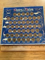 Front view of entire coin set board showing 50 state coins with some missing slots and worn packaging