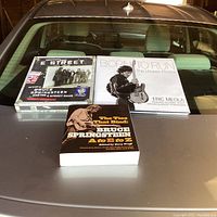 Three Bruce Springsteen books displayed on car hood: "The Ties That Bind: Bruce Springsteen A to E to Z" paperback, "Born to Run: The Unseen Photos" hardcover, and "Greetings from E Street" hardcover scrapbook.