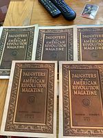 Seven brown embossed Daughters of the American Revolution magazines laid out on a wooden table with visible dates including August and July 1927.