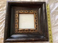 Photo of vintage wooden frame with brass-colored batik style inner decoration and tape measure showing outer frame width at about 11 1/5 inches.