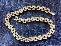 Overall view of the gold tone necklace coiled on textured black background, showing clasp and link design.