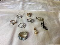 Photo of six vintage rings and three charms on white fabric background showing varying stone conditions including missing stones.