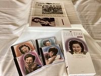 Four CDs in jewel cases along with the 68-page book and the newspaper article replica, all laid out on white fabric.