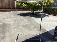 Photo of the white metal rolling clothing rack standing on concrete outside, showing the single hanging bar and base with castor wheels.