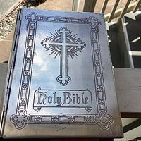 Front cover of vintage Holy Bible with engraved silverplated metal cover showing tarnish and scratches, engraved cross and border design