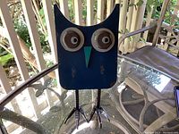Blue metal owl sculpture sitting on glass table showing full front view and bird claw feet.