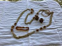 Photo of the vintage amber jewelry set laid out on white cloth. Includes long gold-tone necklace with amber-colored stones, clip-on earrings, and two bracelets.