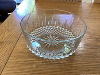 Top side view of clear glass bowl showing starburst and diamond pattern on the sides and bottom, set on wooden table.