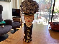 Full view of the Bella Casa head vase "Pearl" on a wooden table, showing the entire figure including the hat and floral dress design.