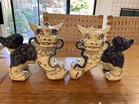 Front view of both foo dog figurines side by side on table against chair backdrop