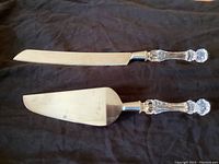 Photo of cake knife and cake server side by side on dark fabric background