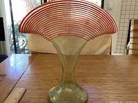 Front view of pale green glass fan-shaped vase with orange striped rim on wooden table.
