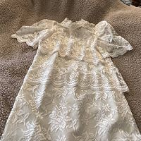 Ivory lace dress laid flat showing lace floral pattern and short-sleeved lace shrug on top