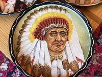 Close-up image of a round metal tray featuring a Native American chief portrait with detailed feather headdress and traditional necklace.