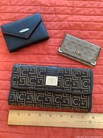 Three different wallets/card holders displayed with ruler for size reference on a red background