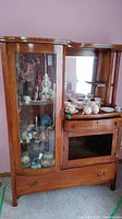 Full view of the vintage wood china cabinet showing glass display door, open mirror section, drawer, and lower cabinet area.