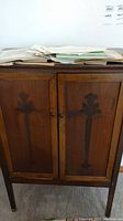 Front view of vintage wooden cabinet with two doors, showing floral carved panels and surface scratches, with papers on top.