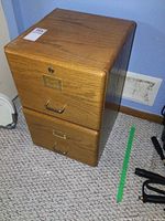 Medium brown wood veneer two drawer file cabinet, showing front with metal handles and label holders, lock on top drawer.