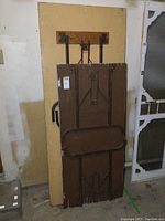 Photo of two folding tables leaning upright against a wall, showing wooden tops with metal folding legs and hardware.