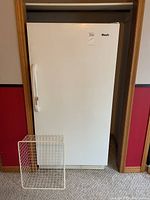 Full view of the white upright freezer with door closed and wire shelf leaning against base