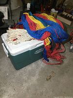 Photo of large Coleman cooler with two colorful hanging hammocks on top, hammock netting in red, yellow, and blue colors.