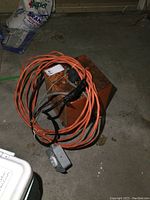 Photo of heavy duty orange extension cable coiled up with black tape around part of it and heavy duty plug attached, resting on a Rusted metal box heater.