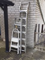 Three aluminum ladders placed against a brick wall and fence, showing full length of the multi ladder and the step ladder.