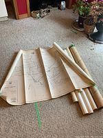 Rolled and unfolded large vintage maps laid on carpeted floor showing detailed black and white geographic details.