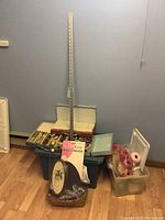 Photo showing multiple bins and containers of needlepoint supplies including spools of thread and stitchery kits near a blue wall.