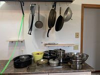 Wide view showing pots, pans, roaster, and various kitchen cookware on kitchen counter and hanging from rod above.