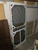 Full view of wooden screen door with white painted frame, decorative corners, and lower spindled section. Screen mesh shows some patched repairs.
