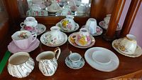 Full set of teacups, saucers, cream and sugar set displayed on dresser with mirror reflecting other items.