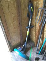 Yardworks electric weed trimmer standing against a wooden wall, with visible power cord and handle