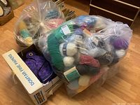 Large transparent bag filled with assorted yarn skeins in various colors and a cardboard box labeled 'Domtar Fine Papers'.
