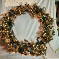 Full view of the 5 foot wide lighted Roosevelt fir Christmas wreath hanging against a white backdrop, showcasing warm white lights and mixed decorative elements.