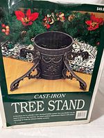 Photo of the boxed picture depicting the cast iron tree stand with holiday decorations in background.