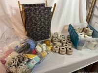 Wide view showing crochet tote stand with floral fabric and a large quantity of crochet thread balls in assorted colors alongside a blue plastic bin