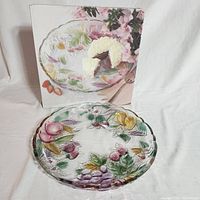 Crystal platter with its original box in the background showing the painted fruit design and cake on the platter.