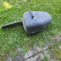 Chainsaw packed in black hard plastic carrying case closed, showing the case shape conforming to chainsaw with bar cover attached.