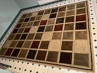 Full view of large area carpet spread on floor showing geometric square pattern in earth tone colors.