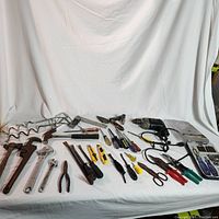 Full layout of various hand tools and power drill arranged on white cloth background showing types and condition of tools