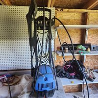 Front view of the Simoniz power washer in a shed, showing the handle, hose, and spray gun attached.